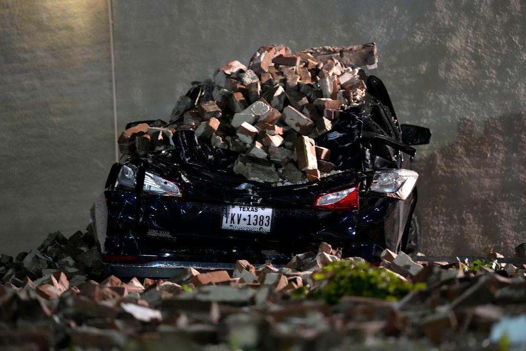 Car crushed by falling bricks from a fallen building wall sits in a downtown parking lot after a severe thunderstorm passed through