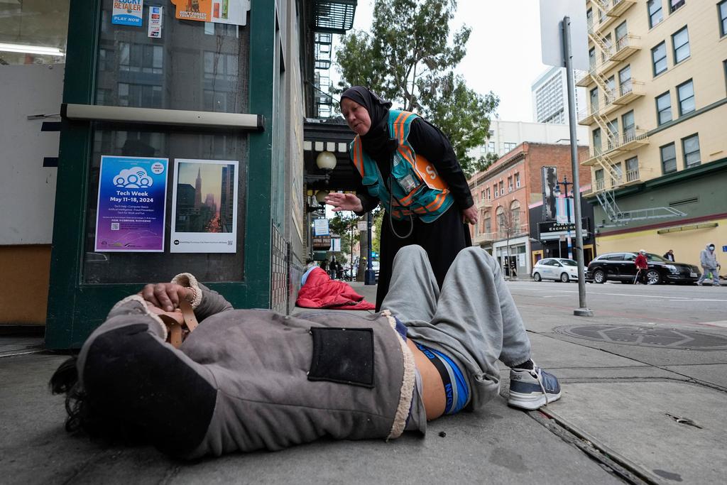 Tatiana Alabsi, right, checks on a man laying on a sidewalk and asks him to please move before children start walking to school in the Tenderloin neighborhood 