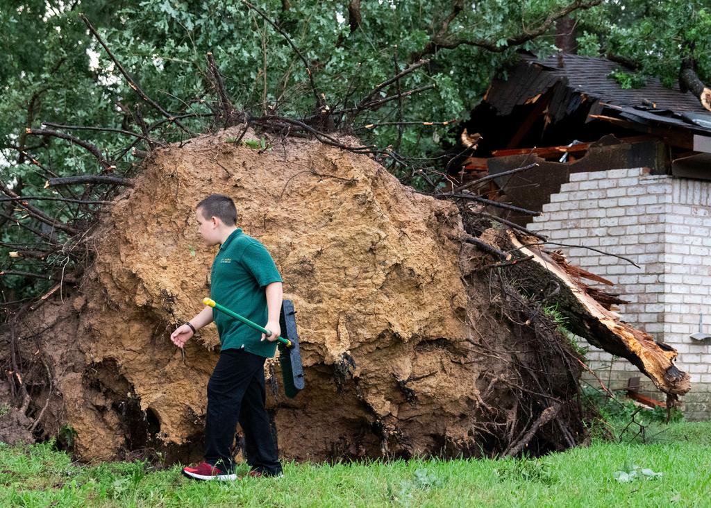 Boy walks past a large tree that fell on a home after heavy wind and rain ripped through the region