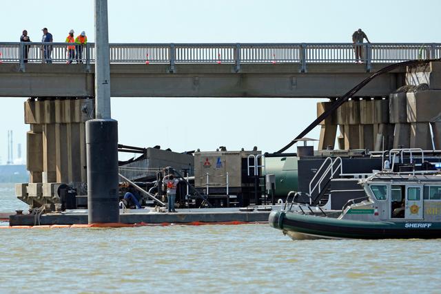 Workers survey the site where a barge crashed into the Pelican Island Bridge
