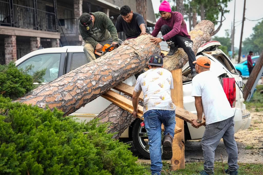 ree service crews climb atop an SUV to cut apart a tree that fell on it at an apartment complex
