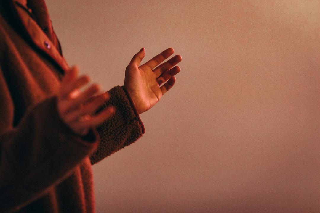 person holding up hands in prayer with orange glow