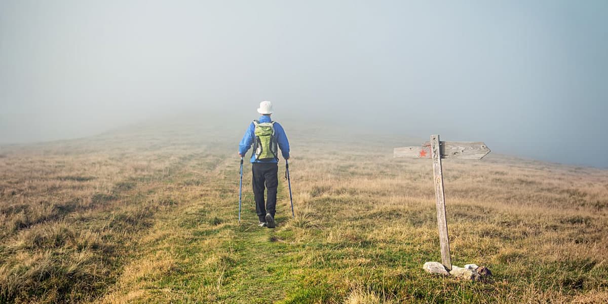 Person hiking into the fog with hiking sticks in hands