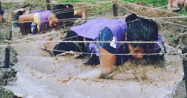 Two women crawling in mud for the Tough Mudder