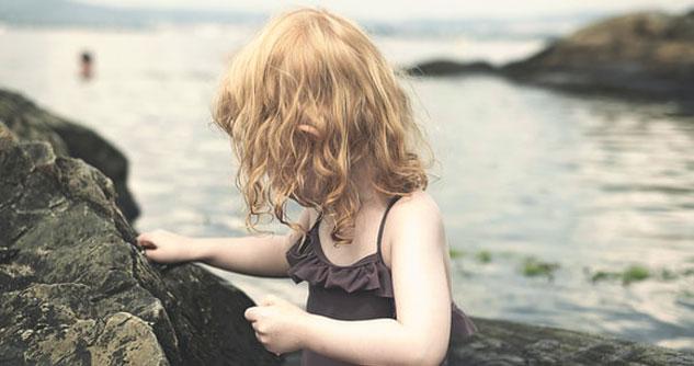 Young girl on rocks at seasdie looks at blurry figure in the water