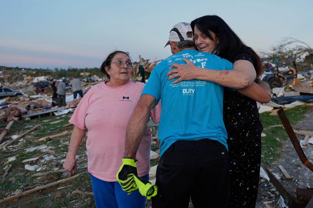 Bea Johnson, left, looks to her sister Kristie Sexton, right, as she is embraced by family friend Keith Adams as they stand next to Sexton's destroyed home