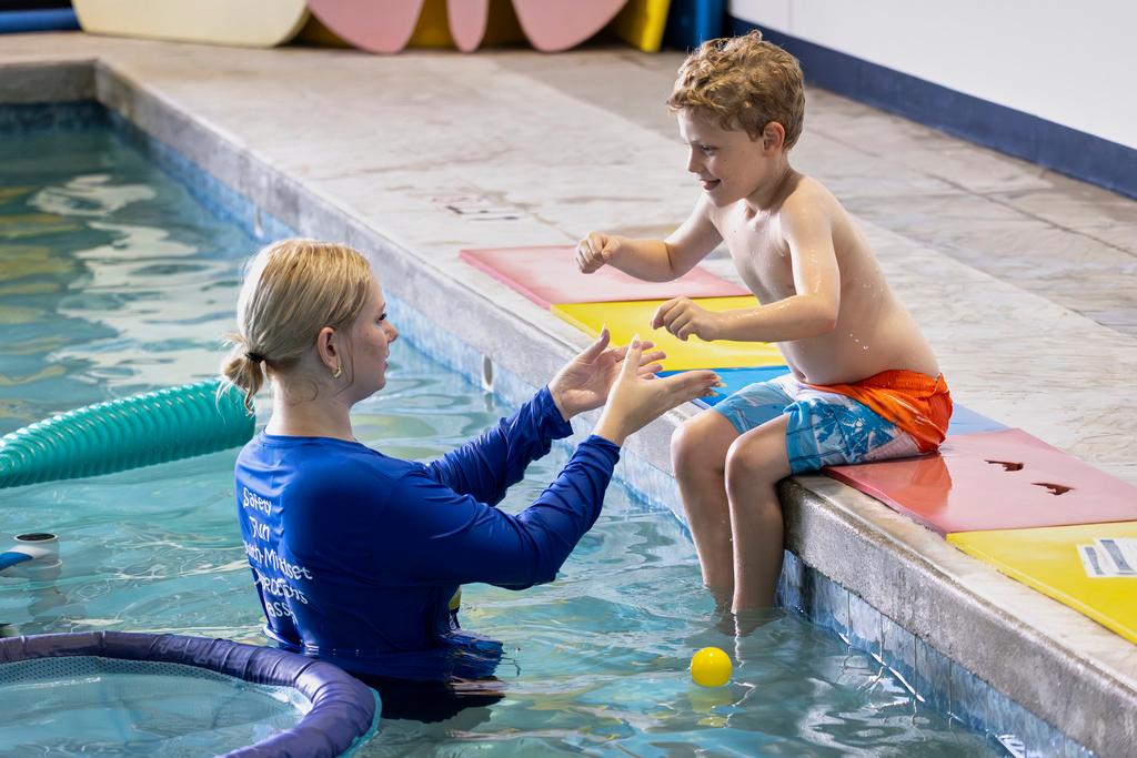 Aquatic educator Riley Taylor helps a student into the water during an autism-specific swim class at Small Fish Big Fish in West Palm Beach, Fla. 