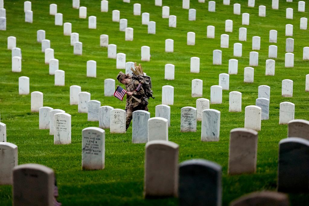 A member of the 3rd U.S. Infantry Regiment places flags at the headstones of service members buried at Arlington National Cemetery, ahead of Memorial Day 2025