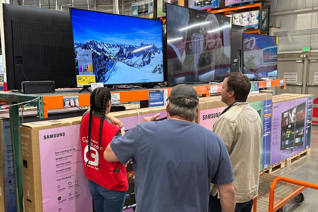 Shoppers consider a large-screen television with the help of a sales associate in a Costco warehouse 