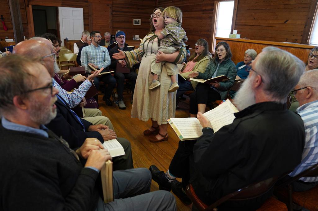 Sarah George, who met her husband through Sacred Harp singing, holds their son while leading a song from the hollow square at a Sacred Harp gathering in Bremen, Ga.
