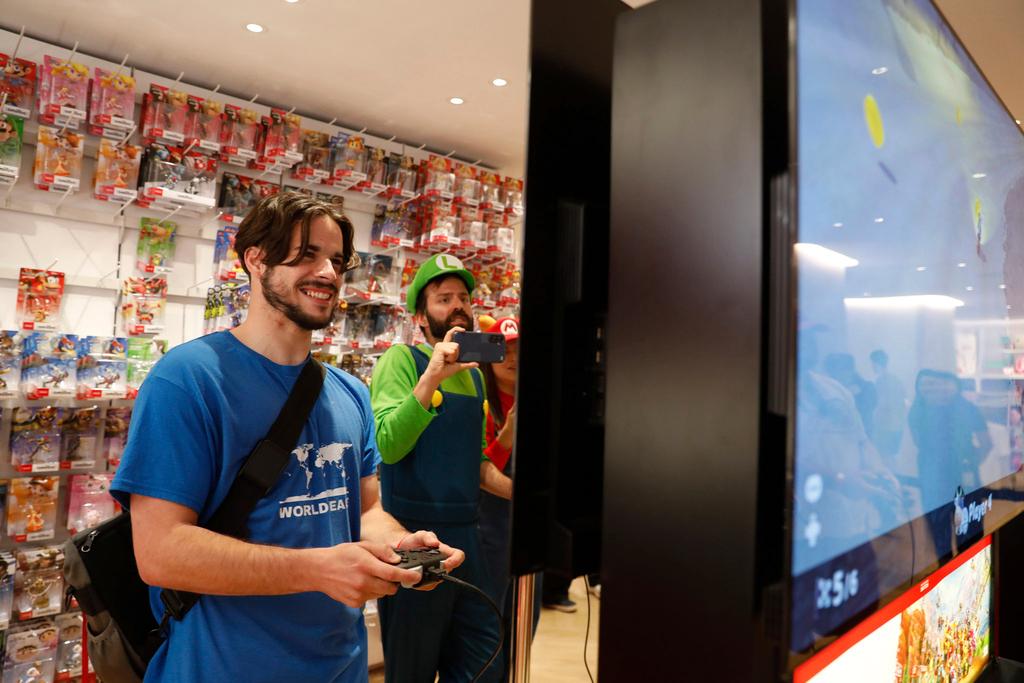 Darren Stallcup, left, of San Francisco reacts as Nicholas Oehlberg, right, of San Francisco documents the event as they play the Mario Kart World for Nintendo Switch 2 game with others at the Nintendo Store for a pre-launch event