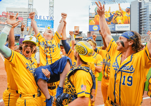 Crowd of Savannah Banana baseball players in yellow with a young boy in their arms
