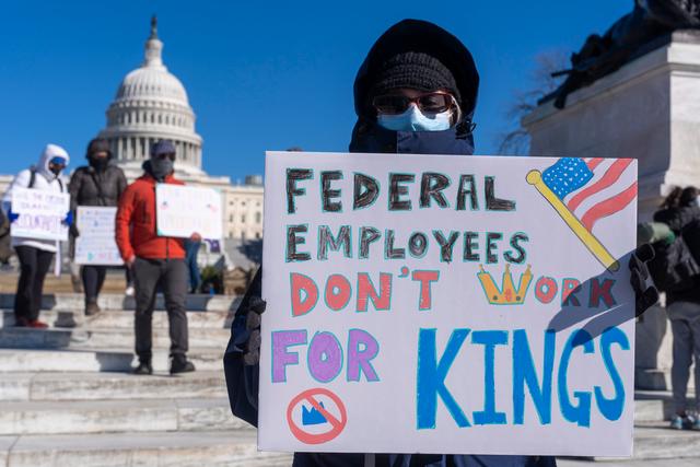 A federal employee, who asked not to use their name for fears over losing their job, protests with a sign saying "Federal Employees Don't Work for Kings" during the "No Kings Day" protest on Presidents Day 