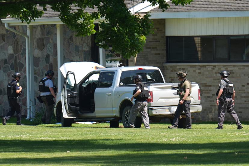 Police walk by an idle vehicle near CrossPointe Community Church in Wayne, Mich.