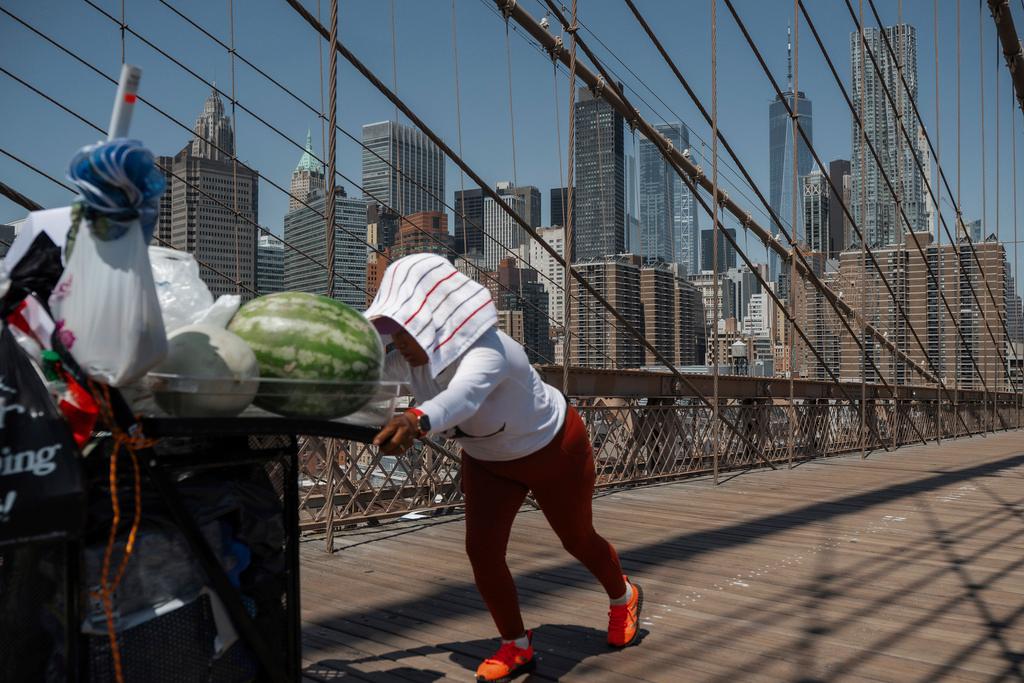 A fruit vendor pushes her cart on the Brooklyn Bridge during a heatwave in New York