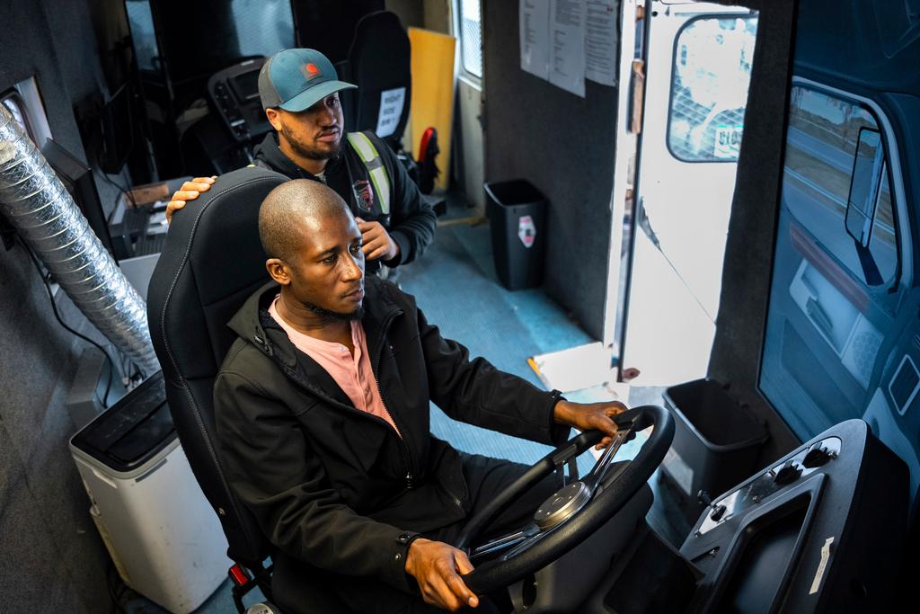Trucking student Mohammed Kamal, left, overseen by instructor Tom Panton, practices driving a tractor-trailer truck in a simulation at the Driving Academy in Linden, N.J.