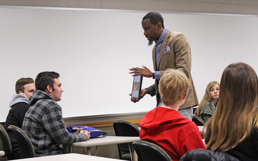 Five students listen intently as Dr. White shares a photo on a tablet device. 