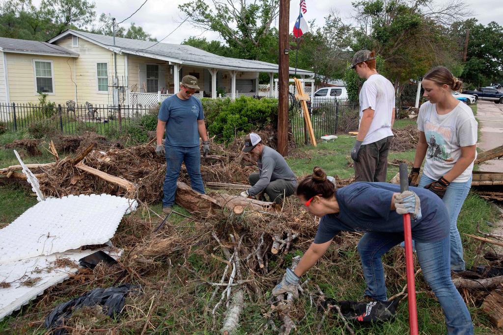 Volunteers from Kerrville Bible Church saw and haul tree debris in front of a flood-damaged home on Guadalupe Street in Kerrville, Texas