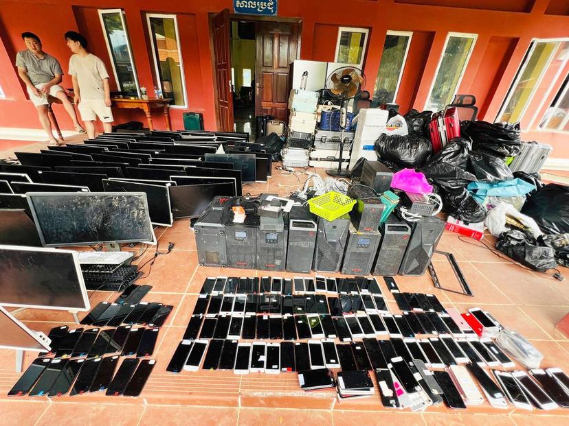 Alleged online scammers stand next to their tools collected by authorities at its site in a classroom 