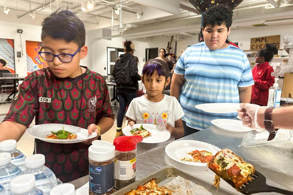 Kids at the after school nutrition program, Milwaukee Public Library Snack Hack, line up to get a slice of pizza made from scratch