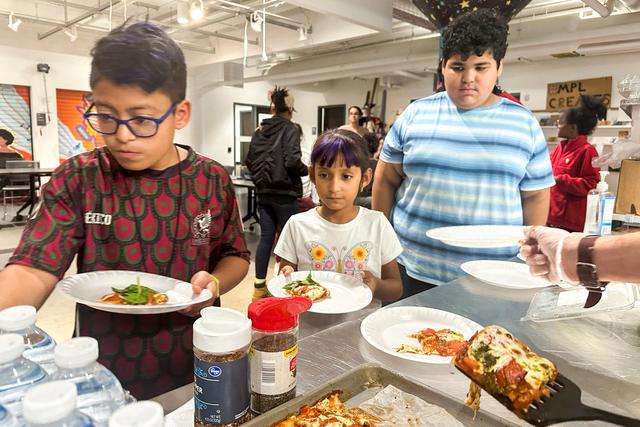 Kids at the after school nutrition program, Milwaukee Public Library Snack Hack, line up to get a slice of pizza made from scratch