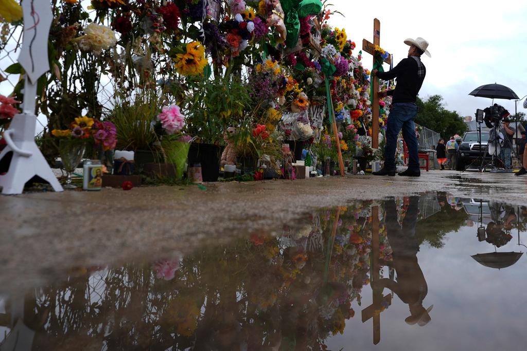 Roberto Marquez places a cross at a memorial wall for flood victims