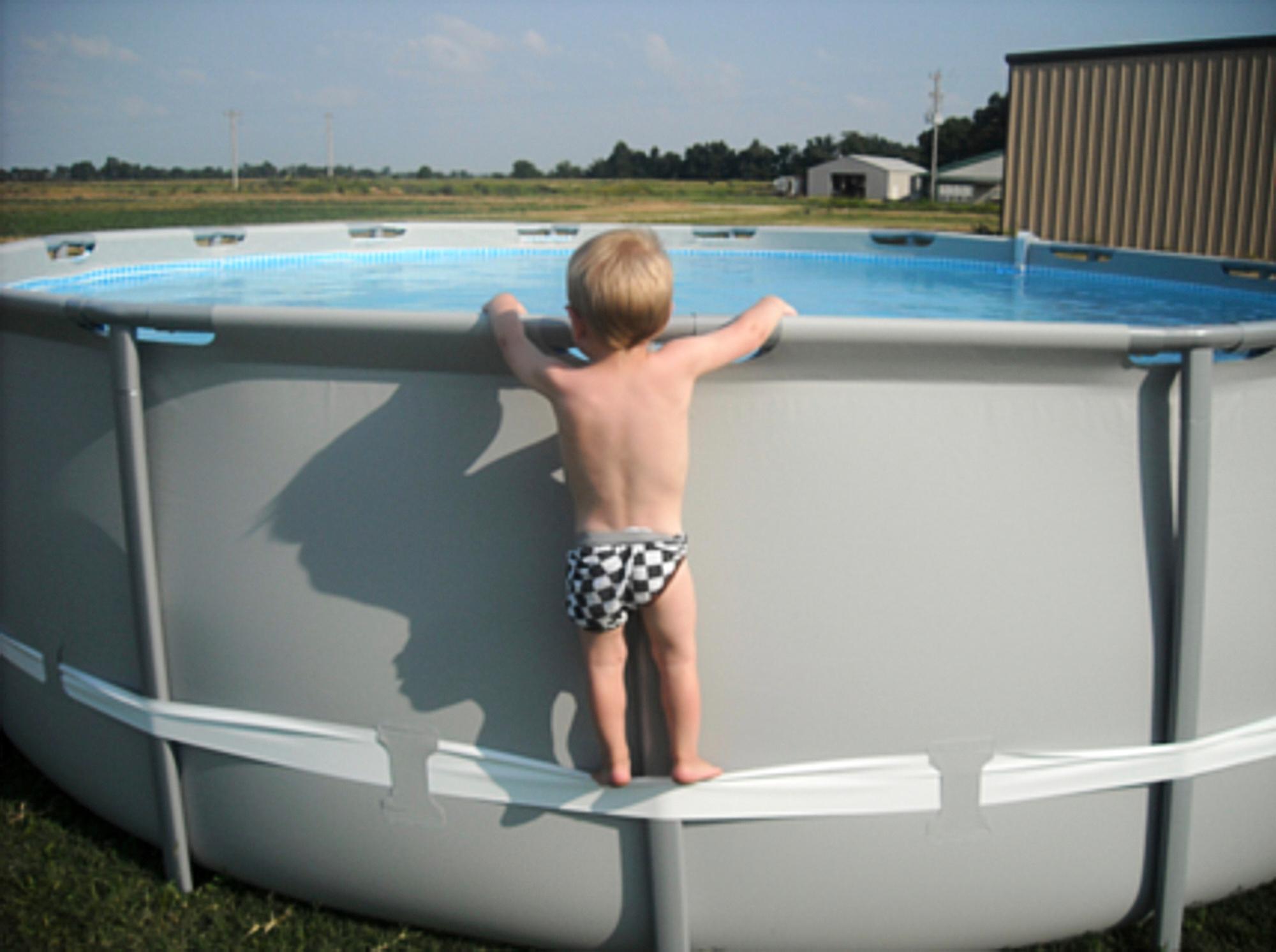 Toddler using side strap to get into above-ground pool.