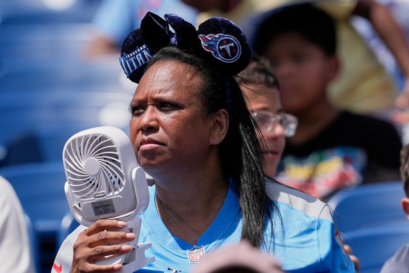 Tennessee Titans fan uses a fan to keep cool while watching practice during "Back Together Weekend" at the team's NFL football training camp 