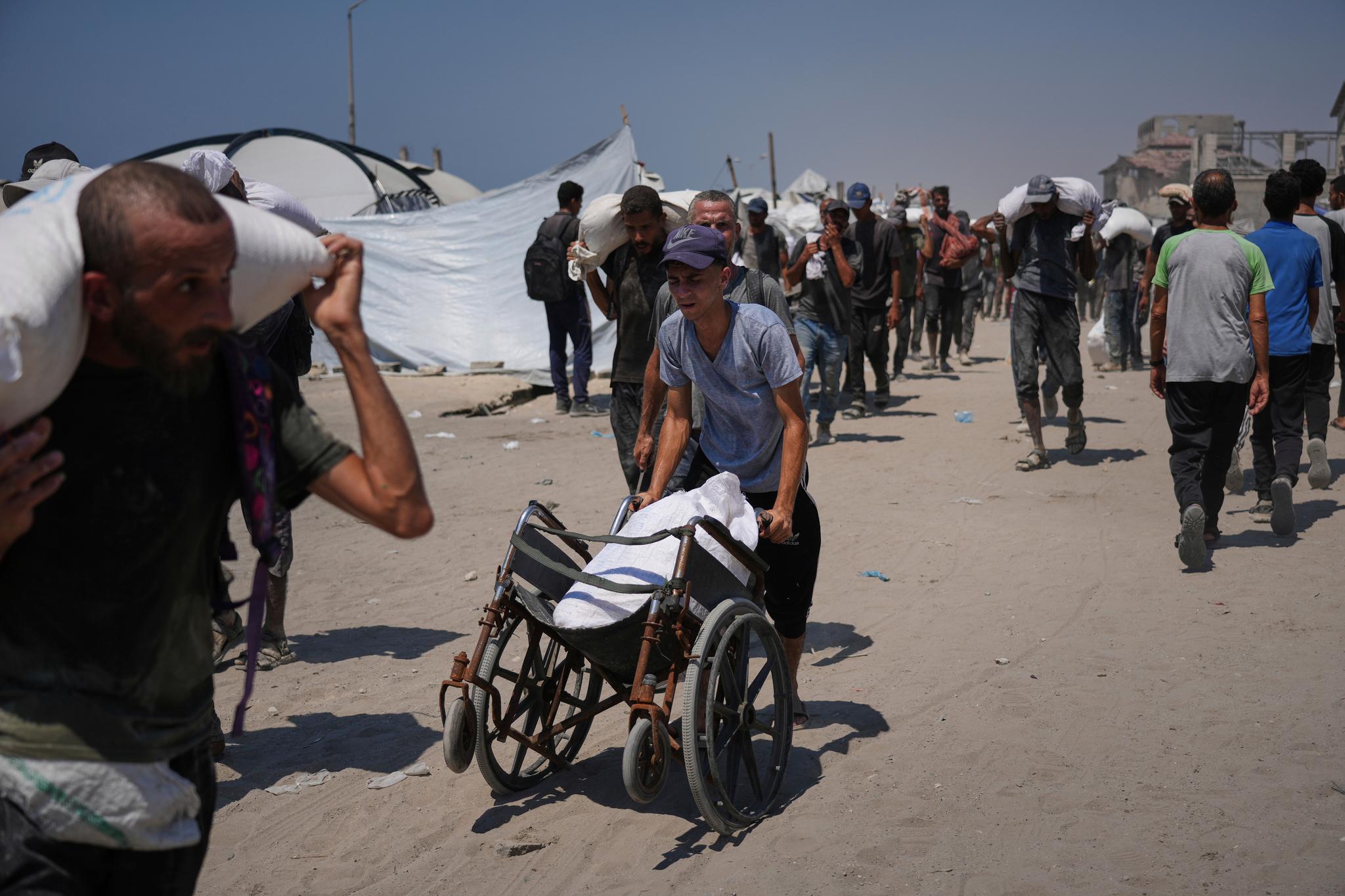 Man wheeling a huge sack of flour in a refugee area with other people carrying bags of flour