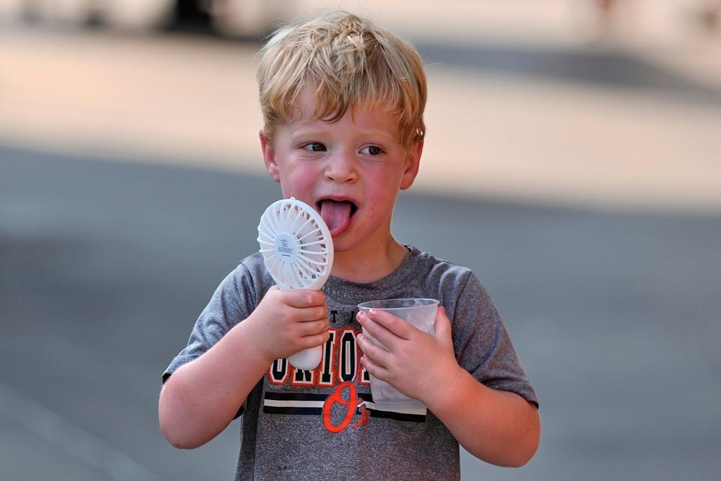  Asher Gillen, 3, uses a battery-powered fan while holding a cup of ice to cool off during hot weather before a baseball game between the Baltimore Orioles and the Texas Rangers