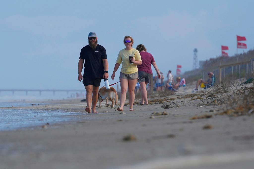 People walk along the beach as waves as red flags, indicating swimming is prohibited, are raised at the beach in Duck, N.C.
