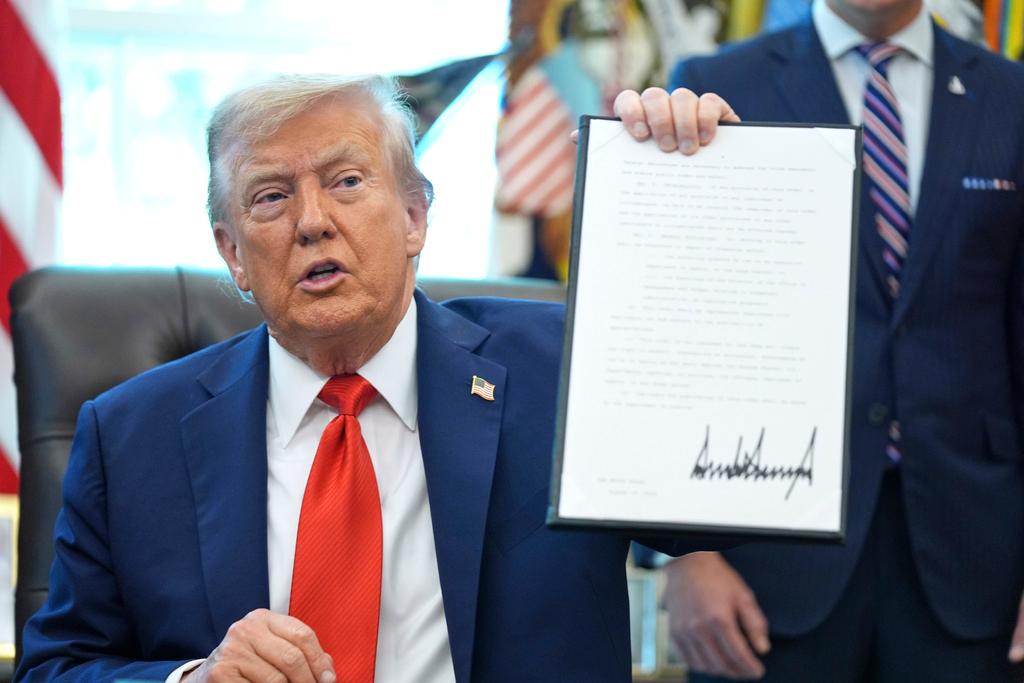 President Donald Trump holds up a signed executive order requiring the Justice Department to investigate instances of flag burning