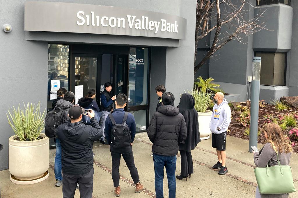 A person from inside Silicon Valley Bank, middle rear, talks to people waiting outside of an entrance to Silicon Valley Bank in Santa Clara, Calif.