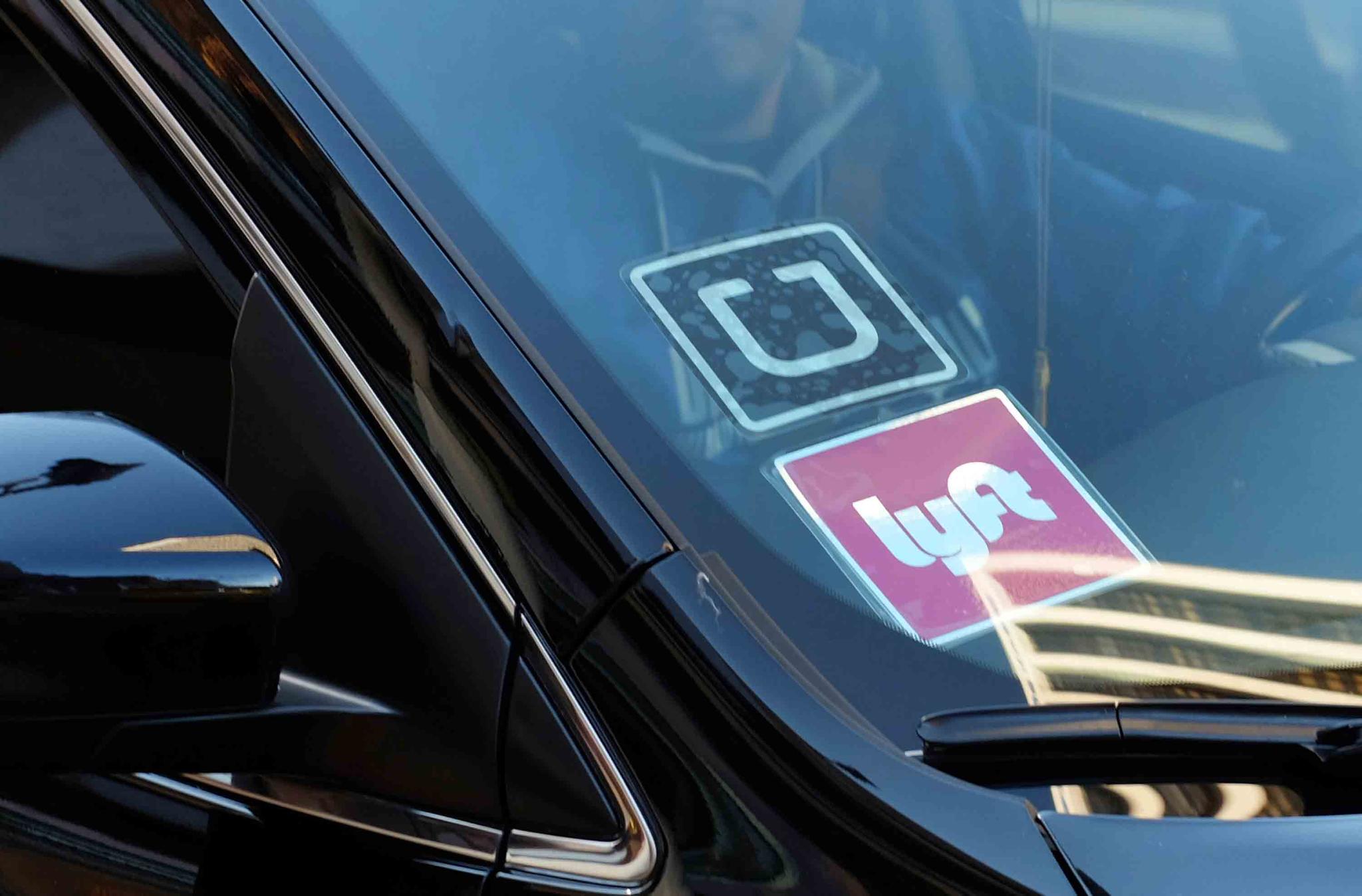 In this Jan. 12, 2016, file photo, a ride share car displays Lyft and Uber stickers on its front windshield in downtown Los Angeles.