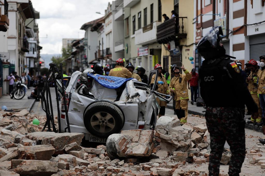 A police officer looks up next to a car crushed by debris after an earthquake shook Cuenca, Ecuador, Saturday, March 18, 2023.