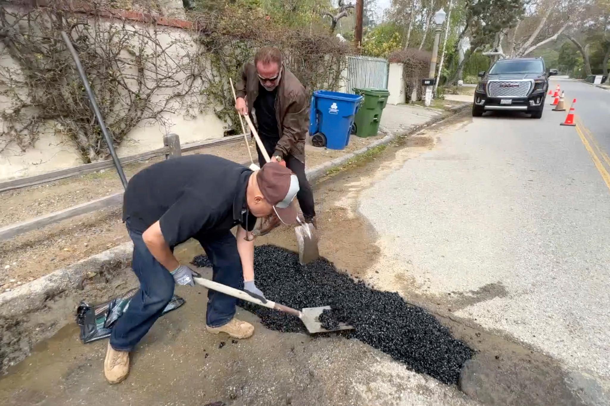 This video still image provided by The Office of Arnold Schwarzenegger, shows former California Governor Arnold Schwarzenegger, center back, repairing a pot hole on a street in his Los Angeles neighborhood on Tuesday, April 11, 2023.