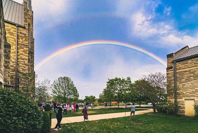 People walking around outside with a double rainbow over the school