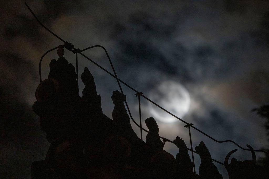 Roof decorations depicting mythical sacred beasts are silhouetted near a penumbral lunar eclipse partially blocked by clouds during the early hours of Saturday, May 6, 2023 in Beijing.