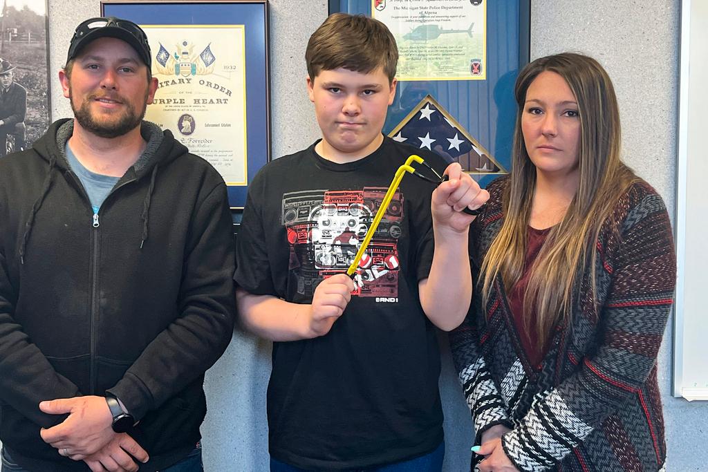 Andrew Burns, left, Owen Burns, center, and Margaret Burns pose with a slingshot Owen used to thwart an alleged kidnapping attempt of his sister, on Wednesday, May 17, 2023, in Alpena Township, Mich. The 13-year-old Michigan boy who used a slingshot to save his 8-year-old sister from an attempted kidnapping on May 10 said he was “freaking out” and simply reached for something that could stop the attack.