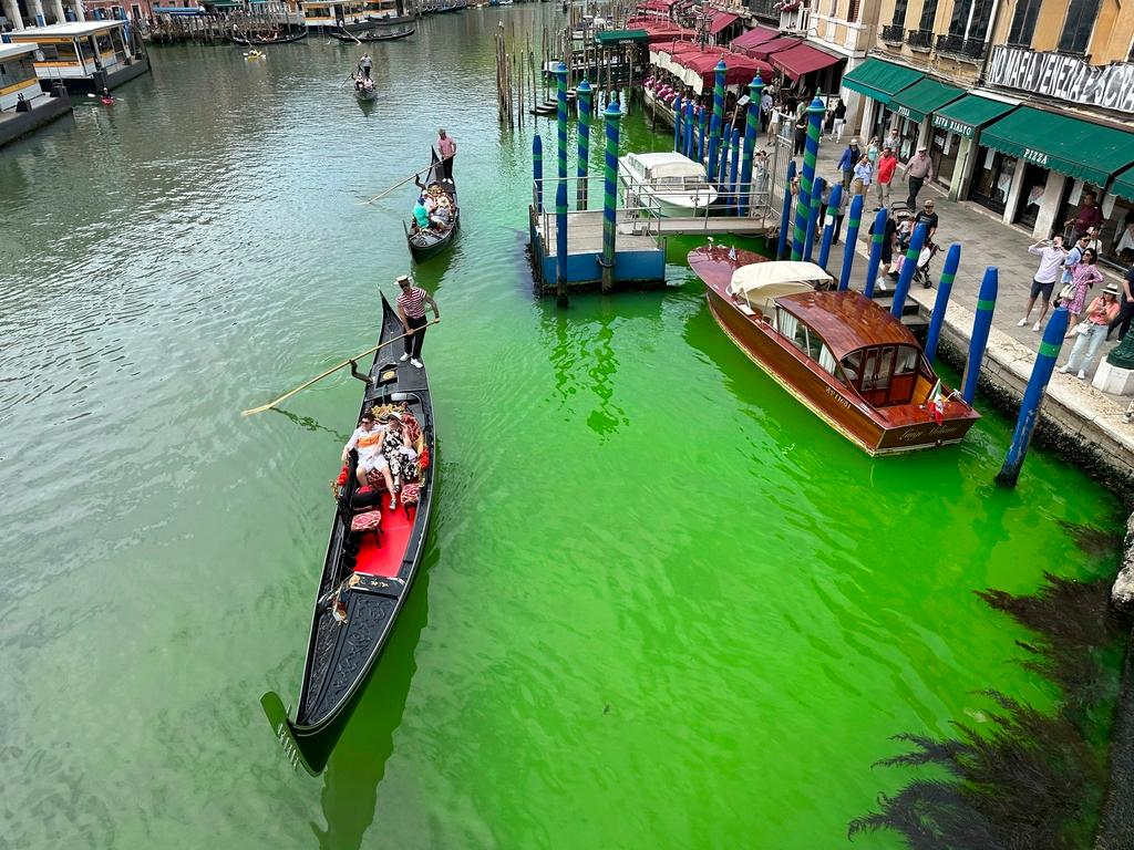 A bright patch of green is seen in the Grand Canal along an embankment lined with restaurants, in Venice, Italy, Sunday, May 28, 2023. Police in Venice are investigating the source of a phosphorescent green liquid patch that appeared Sunday in the city's famed Grand Canal.