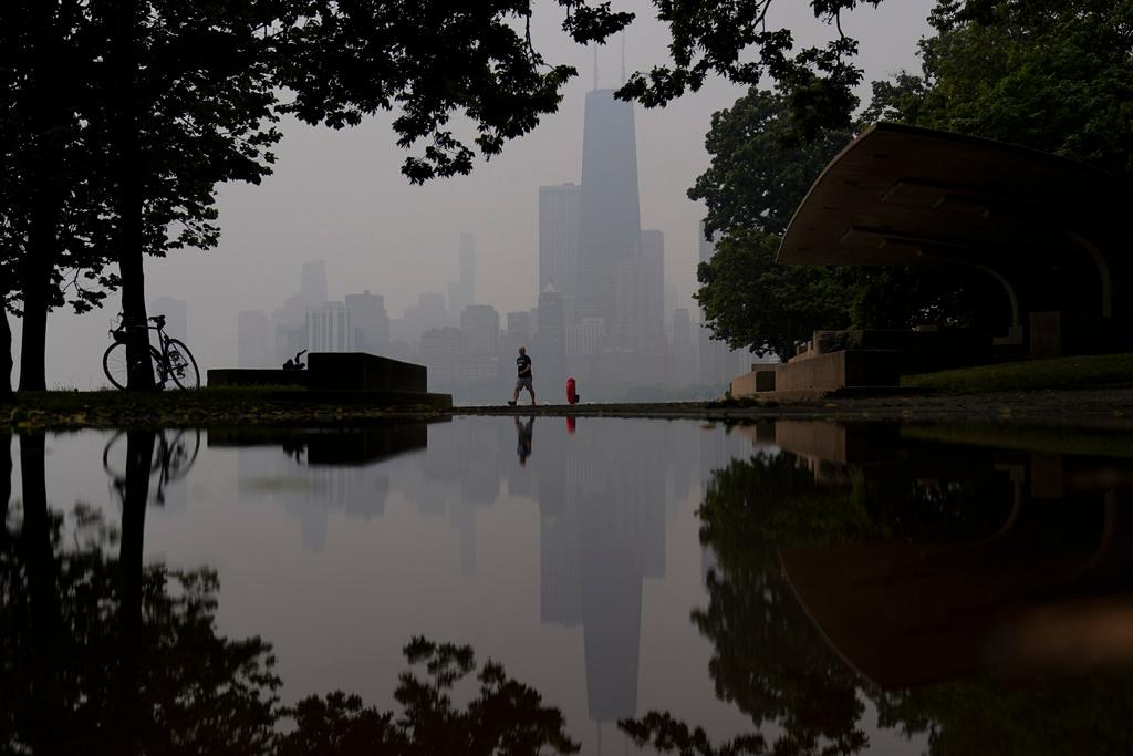 A person walks along the shore of Lake Michigan as the downtown skyline is blanketed in haze 