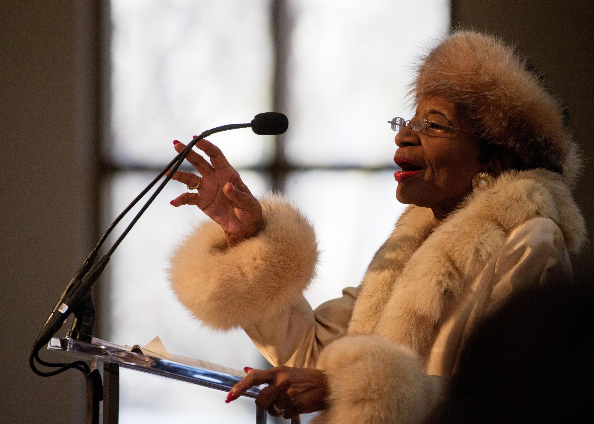 A woman with a fur lined hat and coat speaking at a lecturn