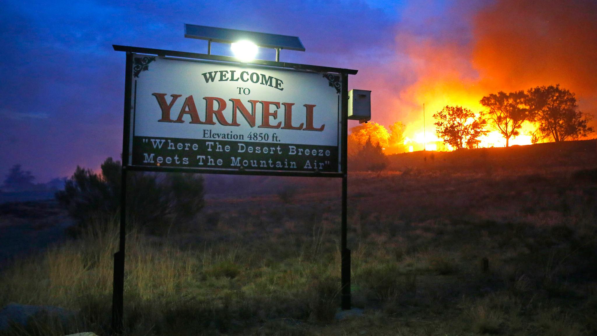 A welcome to Yarnell sign with a fire burning in the background