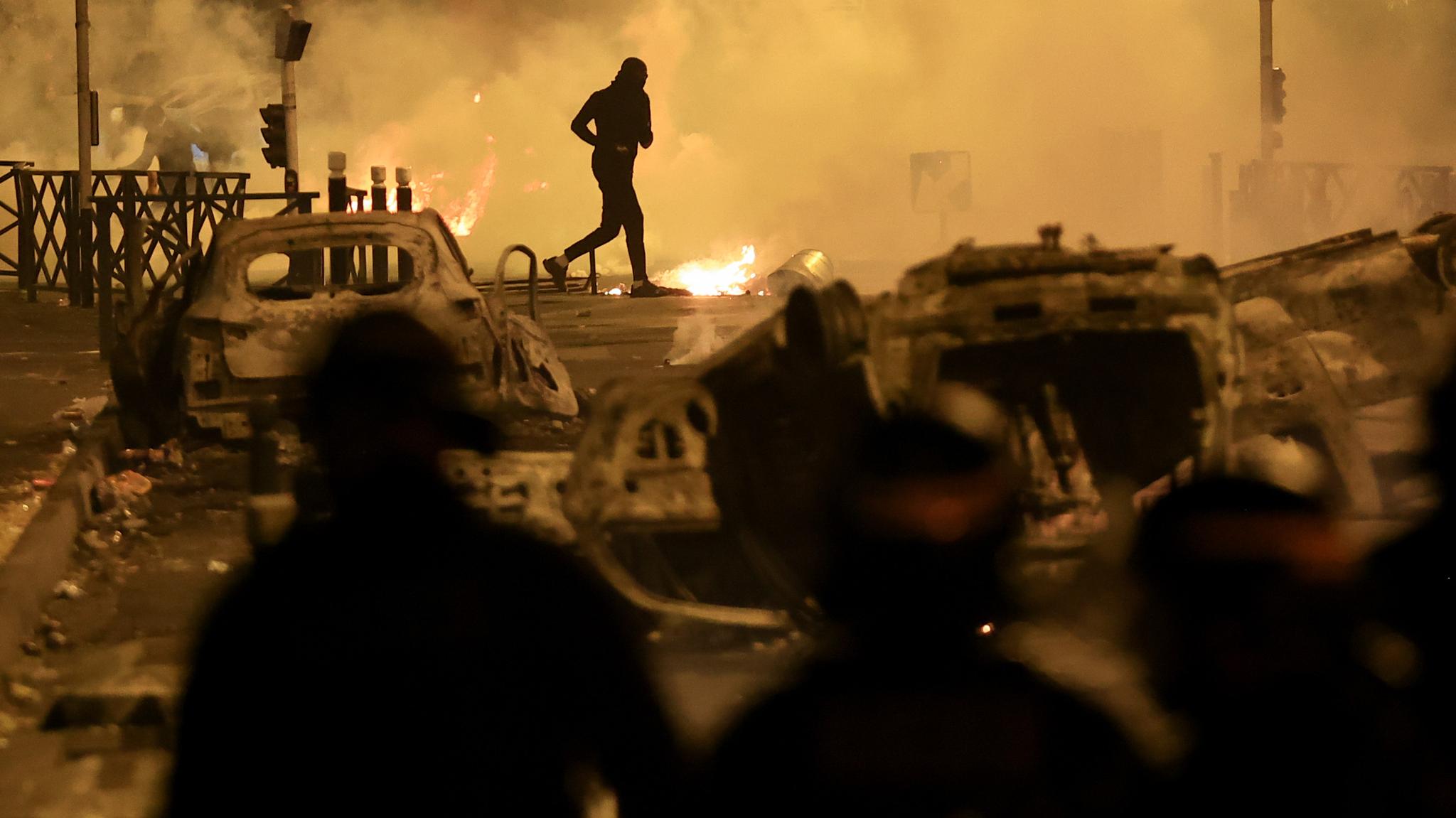 Someone running in the middle of burning cars and piles of trash