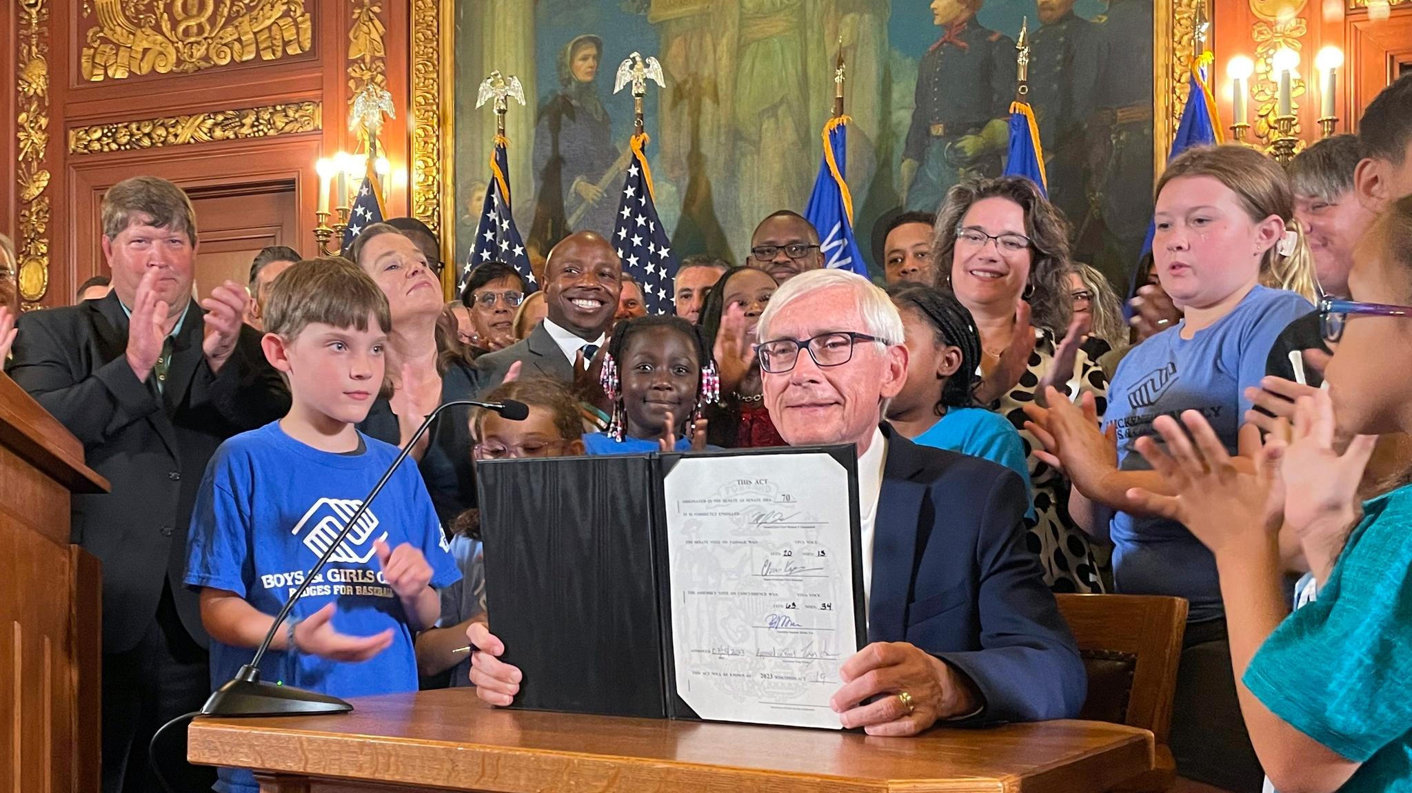 Governor holding up a signed bill with children surrounding him.
