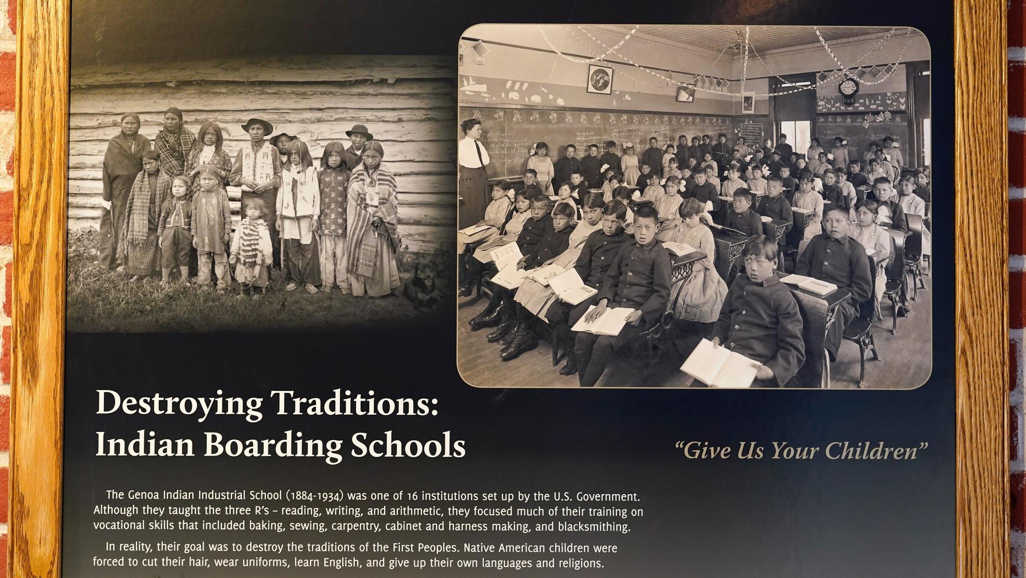 Native American children dressed in western wear and seated in a crowded classroom.