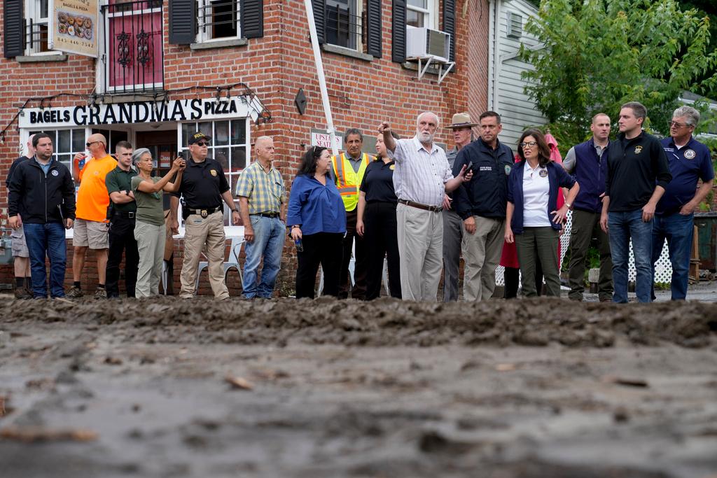 Governor Kathy Hochul, fourth from right, and an entourage of emergency workers, resident, and journalists pass along Main Street damaged the previous day by floodwater in Highland Falls, N.Y.