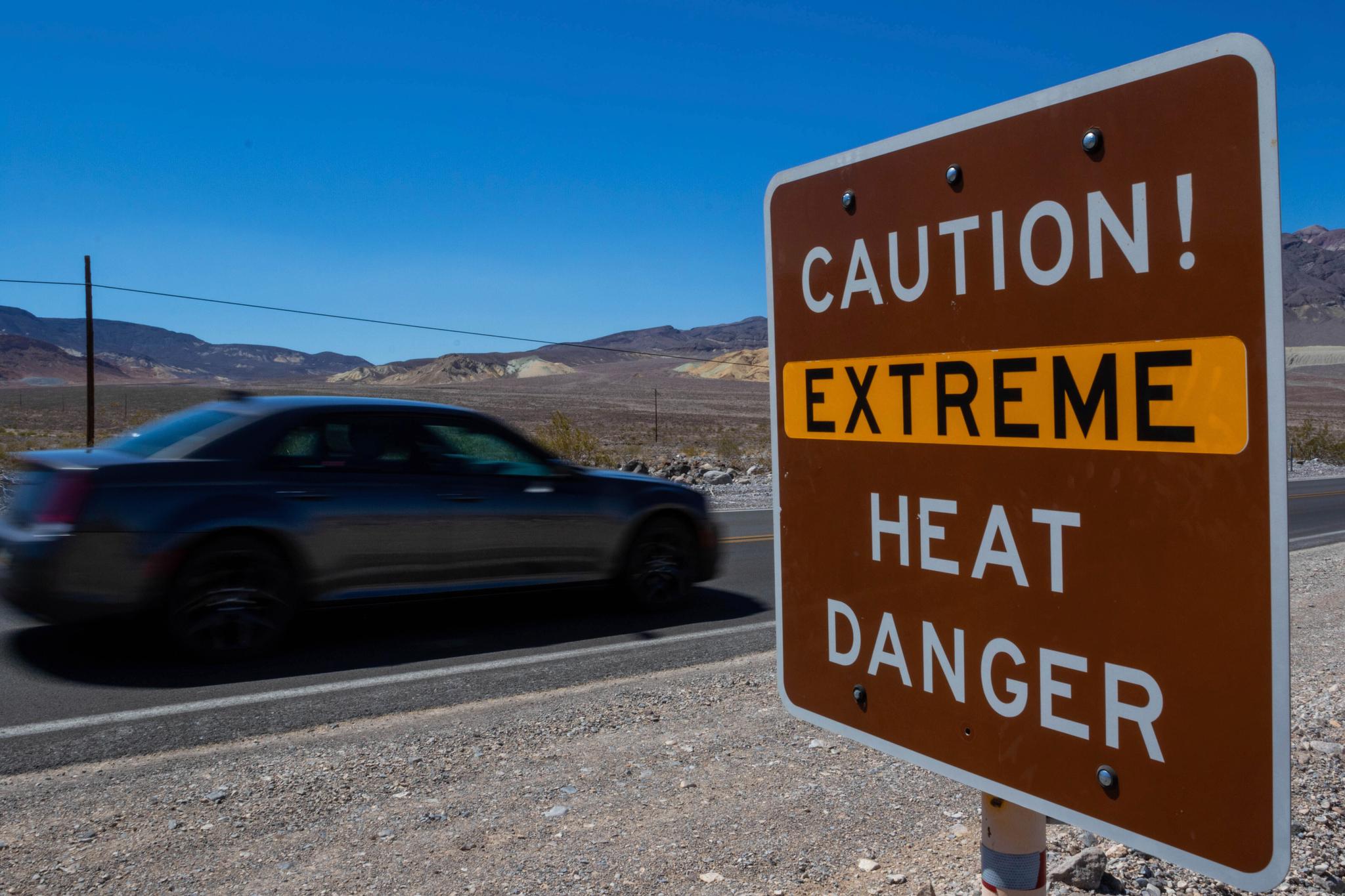 Car driving by sign that says "Caution! Extreme Heat Danger"