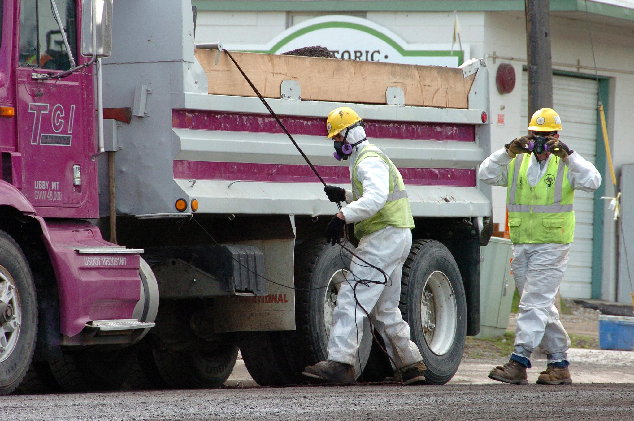 Unidentified road workers wear protective gear against possible asbestos contamination as they load material from a road resurfacing project in downtown Libby, Mont., April 28, 2011. 