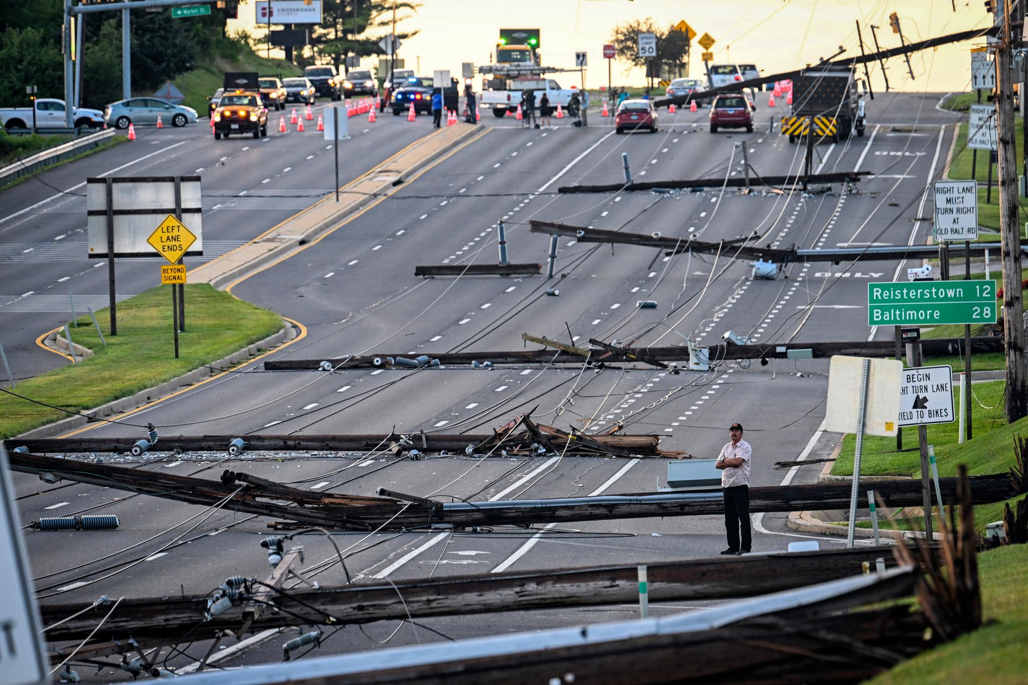 Looking east from Route 97, a man stands in the field of downed power lines and poles on Route 140 in Westminster, Md., Tuesday, Aug. 8, 2023, after powerful storms came through the area Monday evening.